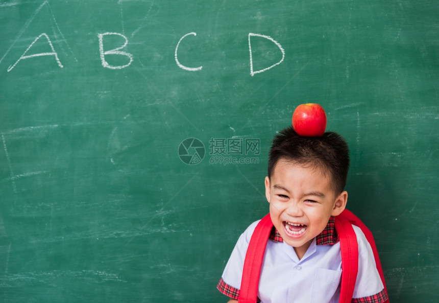 教育文化可爱小男孩穿着校服站在绿色校黑板上微笑图片