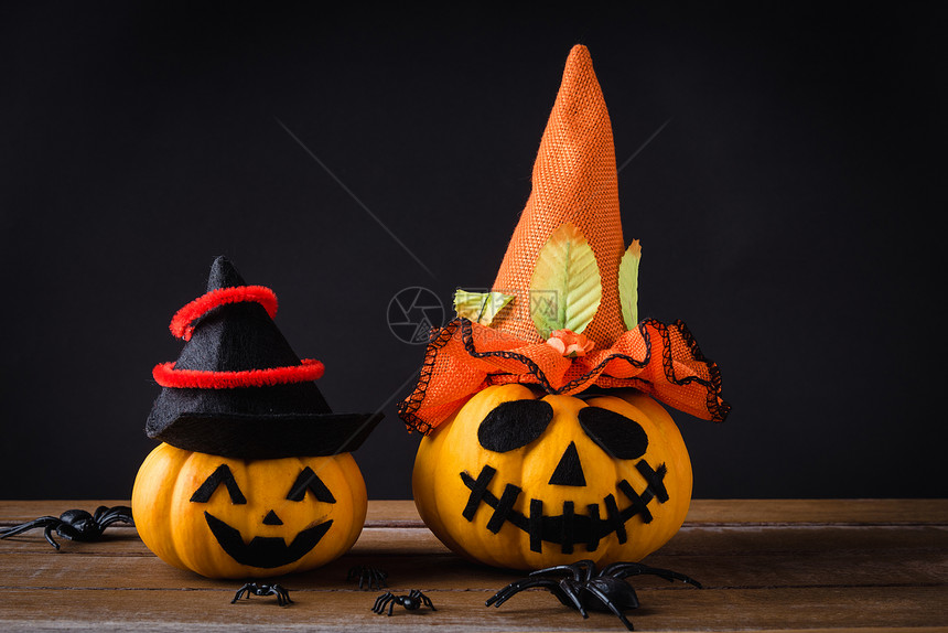 有趣的万圣节派对概念鬼南瓜的头灯插惊吓的笑脸戴着帽子和蜘蛛在木桌黑背景上图片