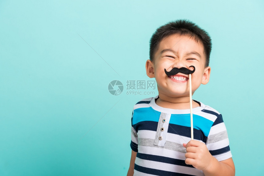 带着黑色胡子道具的嬉笑快乐潮人小孩拿着黑色胡子道具照片亭贴近脸部摄影棚拍着蓝背景的男健康意识前列腺癌图片