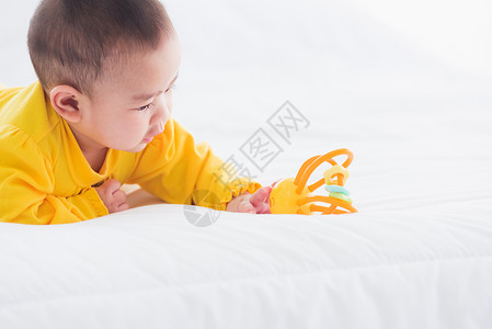 美丽的年轻亚洲新生儿小宝在家中的床上笑快乐的婴儿微穿着黄色衬衫在房间里放松男孩高清图片素材