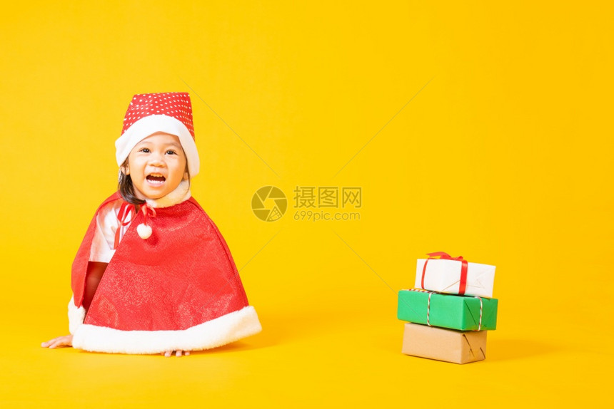亚洲可爱的小女孩笑脸一个穿着红色圣诞老人帽子的孩圣诞节或新年快乐的概念独自坐在黄色背景上图片