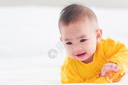 美丽的年轻亚洲新生儿小宝在家中的床上笑快乐的婴儿微穿着黄色衬衫在房间里放松毛巾高清图片素材