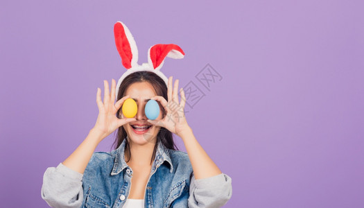 紫背景戴兔耳朵和手拿彩色鸡蛋微笑的女士高清图片