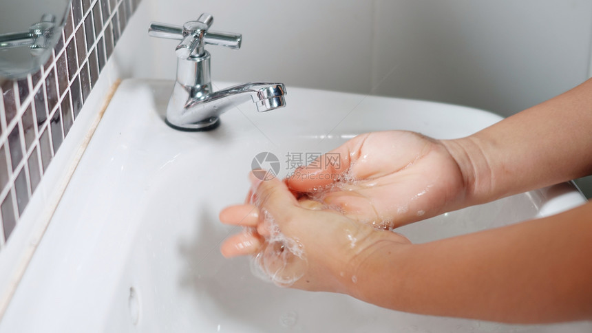 利用肥皂和在水龙头下洗手来拉紧年轻女手在旅馆浴室水槽中用白色泡在洗手池中以保护她免受新冠的伤害图片