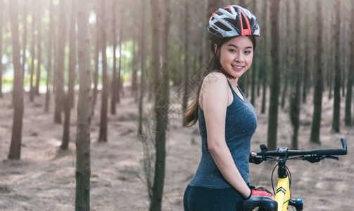 年轻的女头盔夏季在森林里骑自行车带复制空间图片