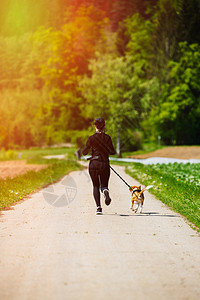 一条狗回家路运动女孩在春天带着一条狗Beagle跑步在通往森林的农村公路上阳光明媚的一天是阳光明媚的一天复制自然空间运动女孩在农村公路上与一背景
