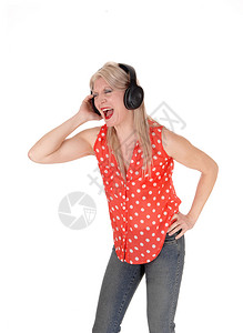 一位美丽的中年女子拿着耳机站张嘴唱歌穿牛仔裤为白种背景被隔离图片