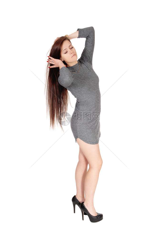 一只美丽的瘦年轻女人站在她长的黑褐发短灰色裙子旁眼睛闭着白底图片