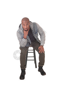 一个年轻英俊的非裔美国人男子坐在椅上手指下巴思考孤立于白种背景图片