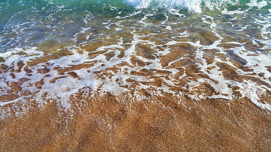 沿海沙砂中带白泡沫的清海水天然封闭背景图片