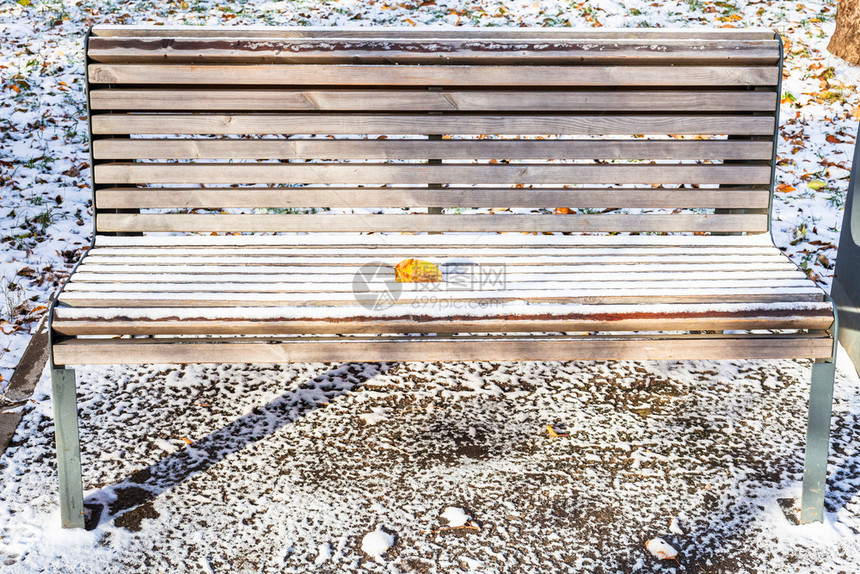 秋天寒冷的城市花园中第一场雪覆盖着落叶的木板凳图片