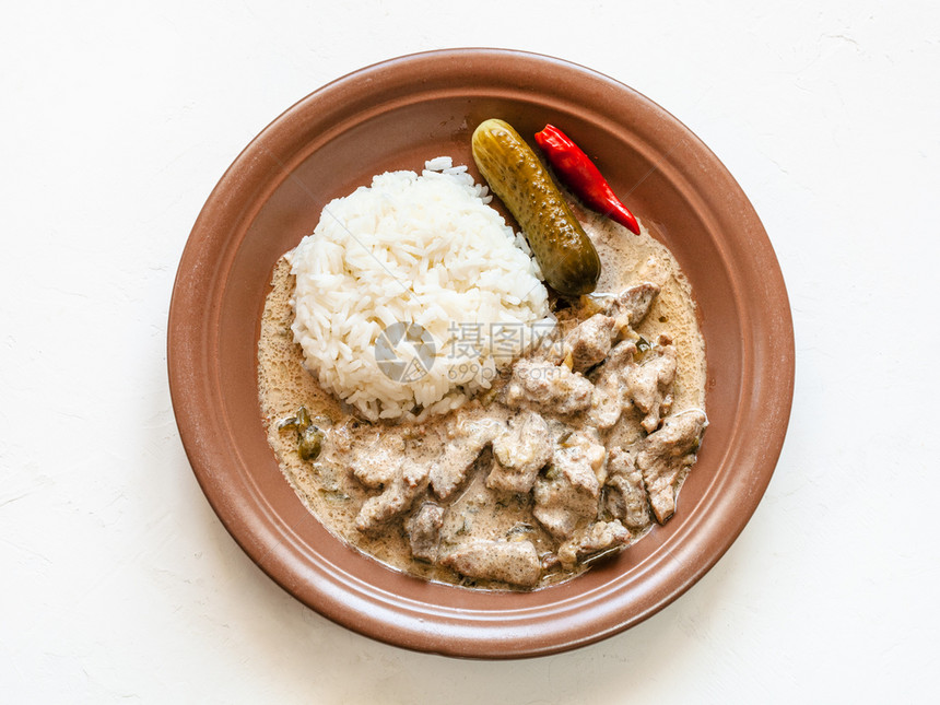 俄罗斯料理白板上棕色盘子上的酸奶油炖肉和煮米饭图片