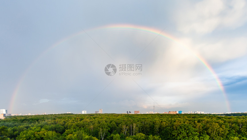 青云天空中的彩虹在阳光明媚的夏夜在绿色森林和城市住宅区上图片