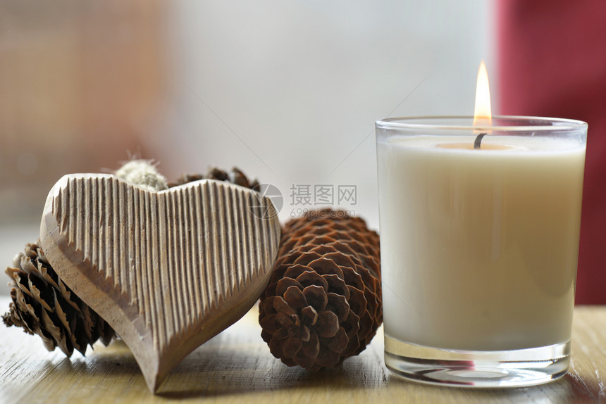 木制心脏与松果对打在室内家的桌子上一根蜡烛旁边的松果下一个木制的庆典图片