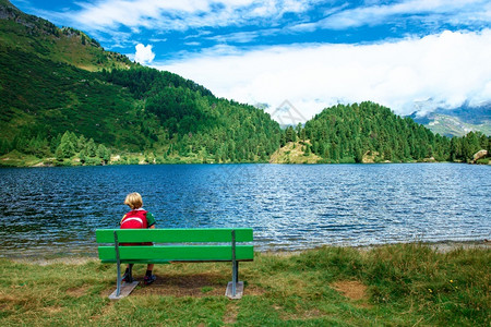 孤独云孩子坐在高山湖前的长凳上一种图片