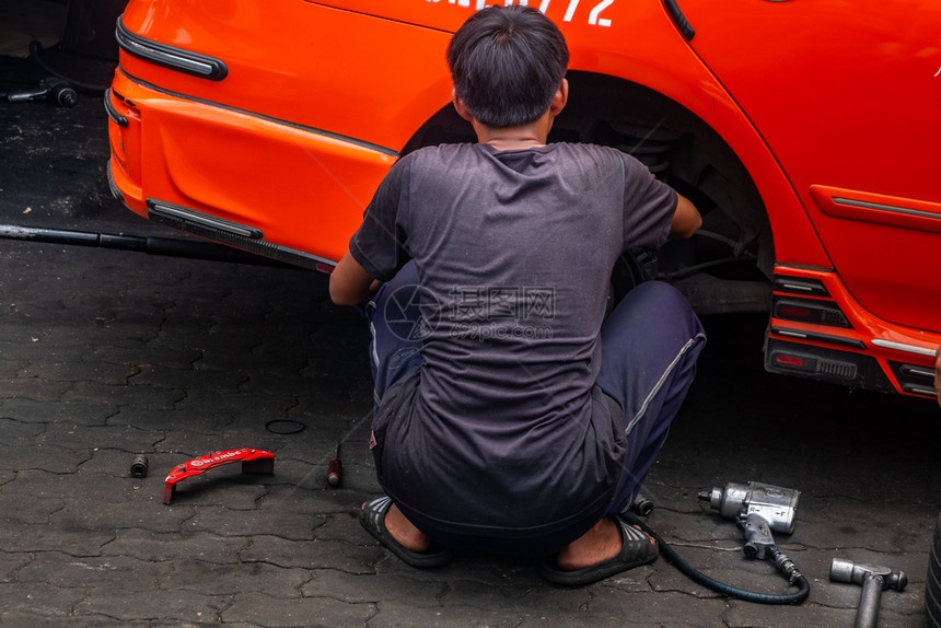 坐着一种黑色的辆穿T恤的机械工正坐在车库前面修轮中枢橙色出租车在库前进行修理图片