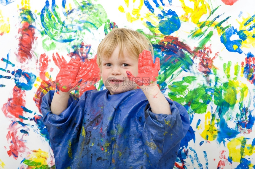 男孩在艺术作品前用红手指涂漆把双蒙上红指彩画的男孩展示给他看的围裙涂片图片