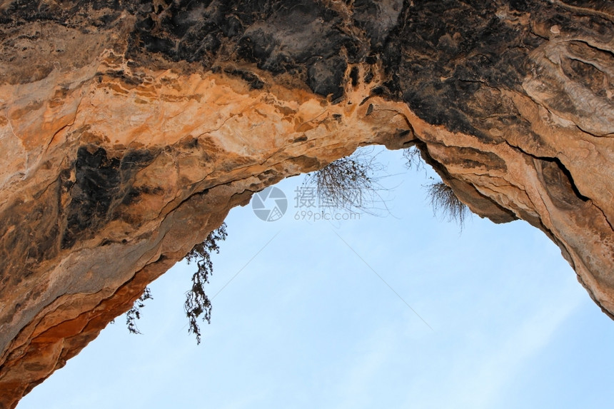 在天空背景上洞穴出口的石形拱门植物灌木丛橙图片