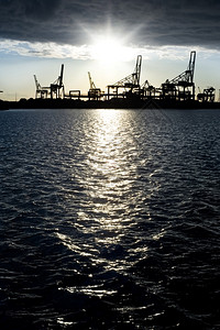 工业的起重机闲港口面对暗冷水中反映的明夕日落时休光轮椅波浪高清图片素材