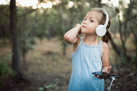 马尾辫脸小女孩在森林里用她的智能手机和耳监听音乐肖像图片