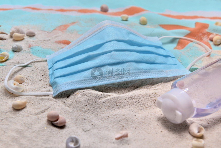 大流行在海滩上贴近蓝色外科手术面具和洗清洁剂的沙滩上与covid19一起的概念度假毛巾药物图片