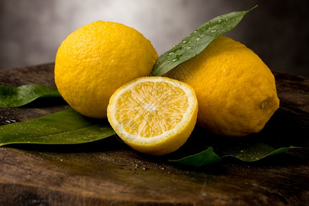 鲜黄柠檬照片木制桌上有叶子和水滴新鲜的生柑橘图片