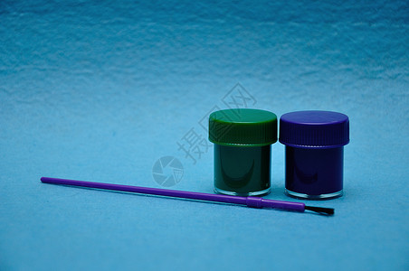 绿色锅婴儿两罐涂料蓝色背景的紫油漆笔刷图片