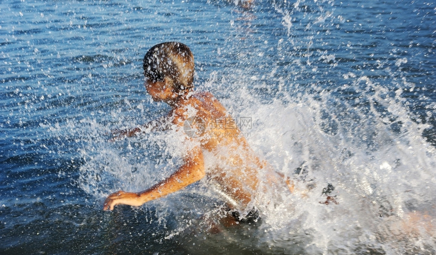 一个男孩在Kinneret湖温水中玩耍溅快乐的晒黑图片