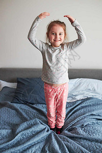 有趣的愉快乐小玩女孩得开心做傻笑的脸在床上跳早卧室家微笑图片