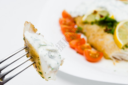 石斑鱼肉盘子白上加蔬菜和奶油酱的烤鱼图片