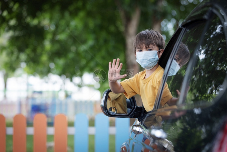 年轻的正面小可爱男孩穿着面罩身戴坐在车窗后从前座上车窗撞出孩子在科罗纳大流行疾期间返回学校保护图片