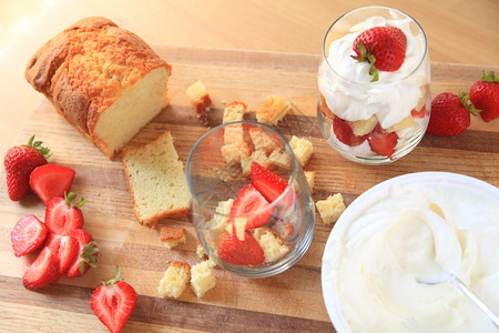 对待新鲜的草莓奶油和磅蛋糕的盖头在切割板上装有成品的微型小块纸眼镜图片
