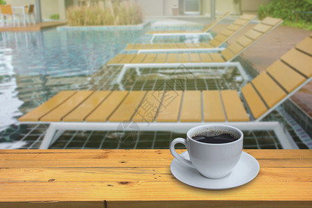 碟子池畔木地板上一小杯咖啡和模糊游泳池底木制的图片