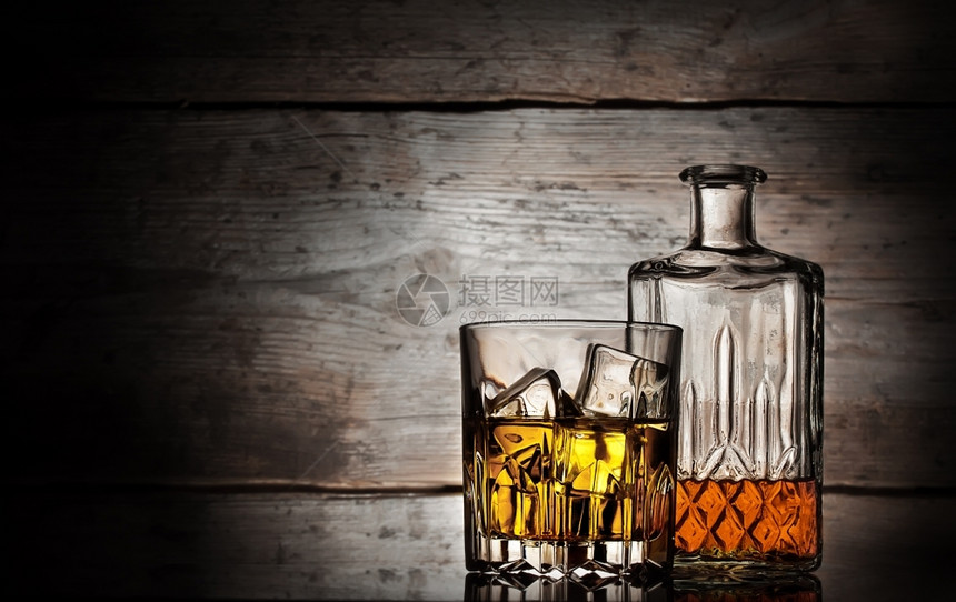 科涅克白兰地玻璃优雅一杯威士忌加冰块和面罩瓶子在木制背景上图片