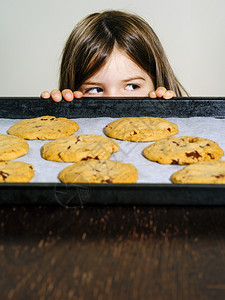 盯着可爱的托盘一个年轻女孩看着一盘温暖的巧克力片饼干照图片