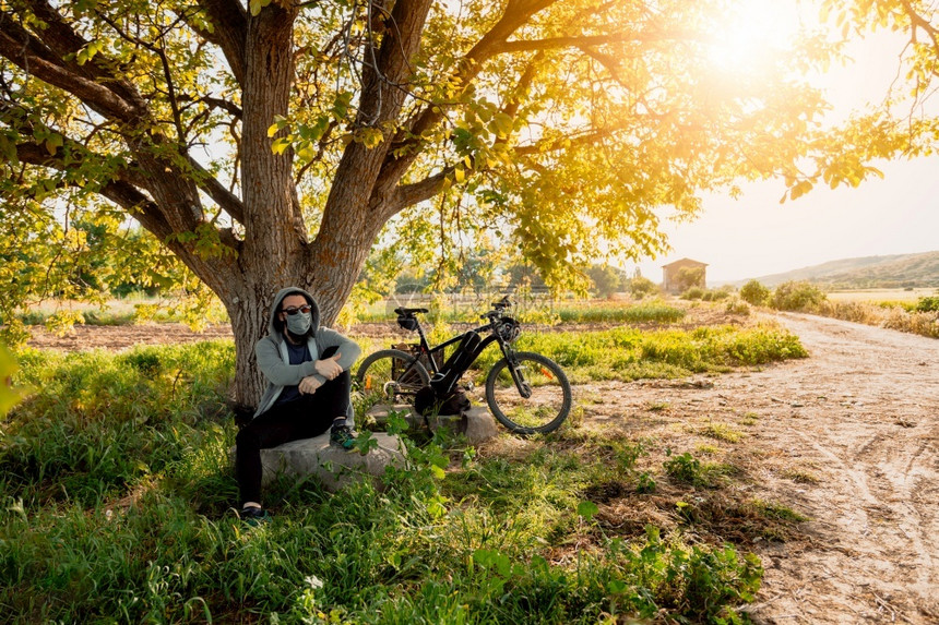 阳光大流行户外男人在野戴科面罩脚踏自行车在西班牙被共生19岁时降温图片