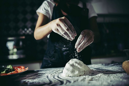 桌子自制厨房妇女将面粉倒在团上而手鼓则准备做比萨饼烹饪概念图片