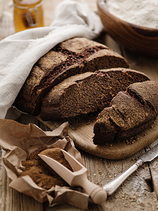 在配有麦粉和面的木制桌上在一张木自制切碎的圆黑麦面包健康烘烤的切片图片