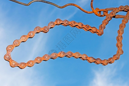 技术的双环旧生锈钢链挂在对蓝天的铁丝网上曲线背景图片