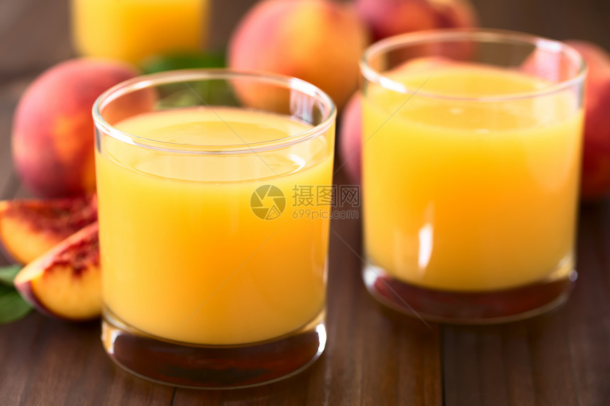 正面杯子中的桃汁或花蜜背面有新鲜成熟的桃子水果在深木上拍照有自然光选择焦点关注玻璃边缘的前端以及第一杯桃汁或果第一的背部图片