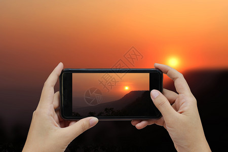 白色的移动女手持智能机在日落山脉的模糊背景上用白空屏幕遮住智能手机图片