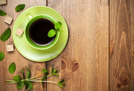 新鲜草本黑色的茶叶薄荷绿色杯中含薄荷叶和棕色糖木本底背景图片