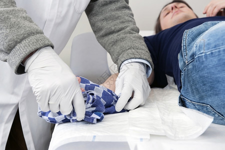 医疗的一种生从位躺在急救室检查桌上的病人受伤手上解开一条茶巾将毛从一个受伤的病人手上撕开援助背景图片