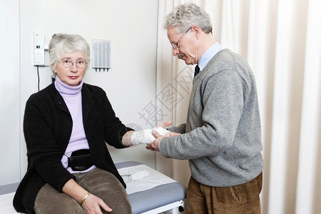 医生在院急救室检查一名老年妇女的绷带扭伤手腕并进行体检伤害房间听诊器背景图片