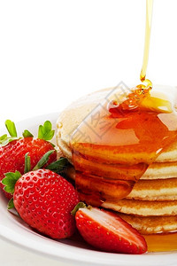 蓬松的酪红色金糖浆在热黄油煎饼上流下面加了草莓装饰品背景图片