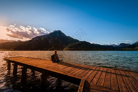 日落时坐在湖边木制码头栈道上的人图片