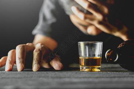 微醺小醉成人在一个男子醉酒时将一个小玻璃杯中的酒精放在黑桌子上而一个男则坐在醉酒状态下郁闷孤独背景