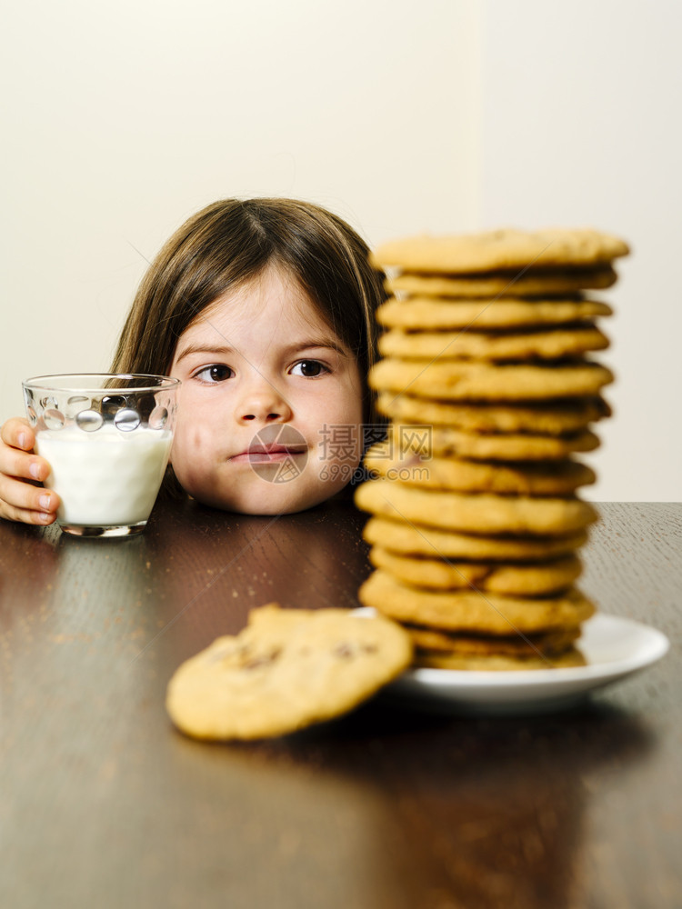 食物微笑照片中一位年轻女孩在握着一杯牛奶时凝视着一堆巧克力曲奇饼干的巨型巧克力花栗饼脸图片