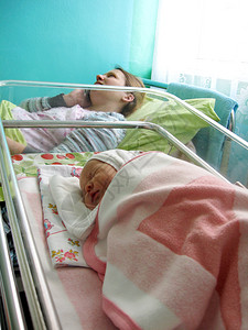在妇产医院带新生儿的妇女妈和在产医院的新生婴儿躺在小床上妈得到祝贺出生门户14健康怀孕高清图片素材