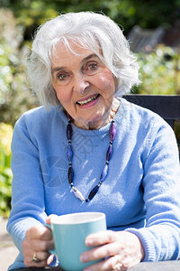 在花园中喝热饮放松的老年妇女肖像微笑享受坐着图片